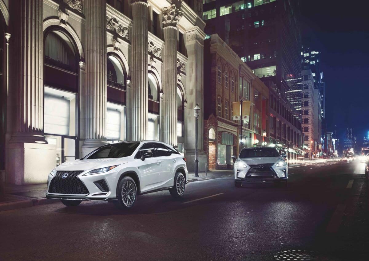2022 Lexus RX 450h luxury hybrid SUV models on a city street lit with night lights and traffic