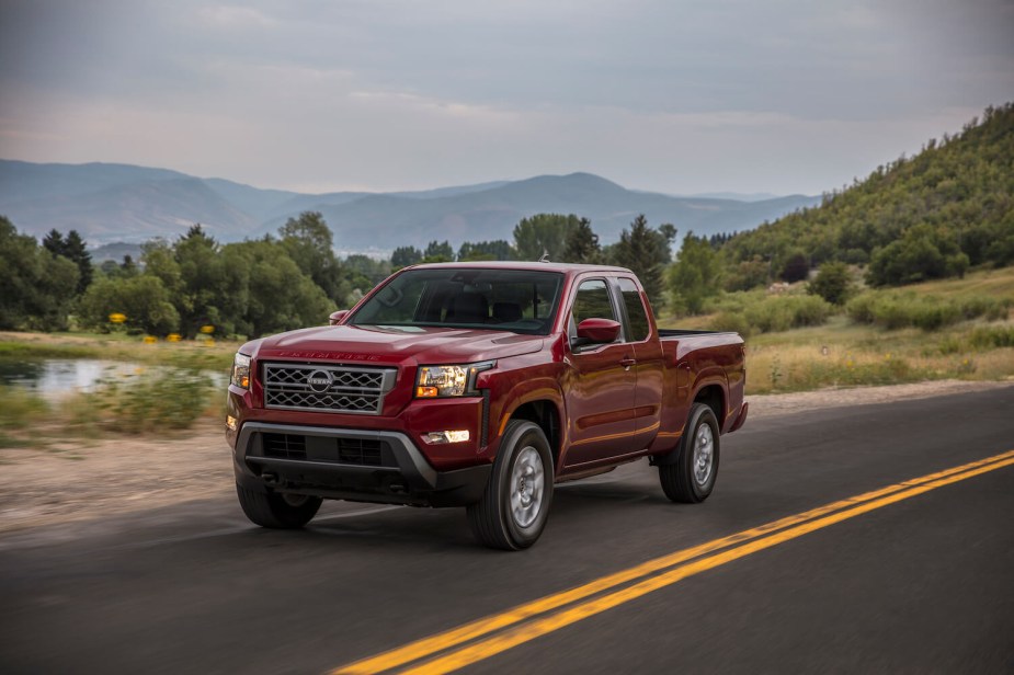 Promo photo of the redesigned 2022 Nissan Titan midsize pickup truck driving down a country road, trees and mountains visible in the background.