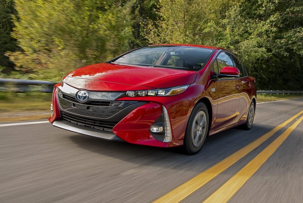 A 2022 Toyota Prius Prime PHEV blasts down a back road in bright red.