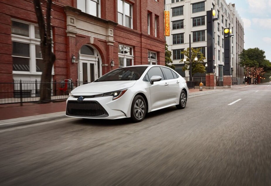 A white Toyota Corolla Hybrid shows off its four-door car practicality and hybrid efficiency as it drives down a city street. 