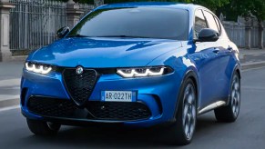 A blue 2023 Alfa Romeo Tonale subcompact plug-in hybrid luxury SUV is driving on the road.