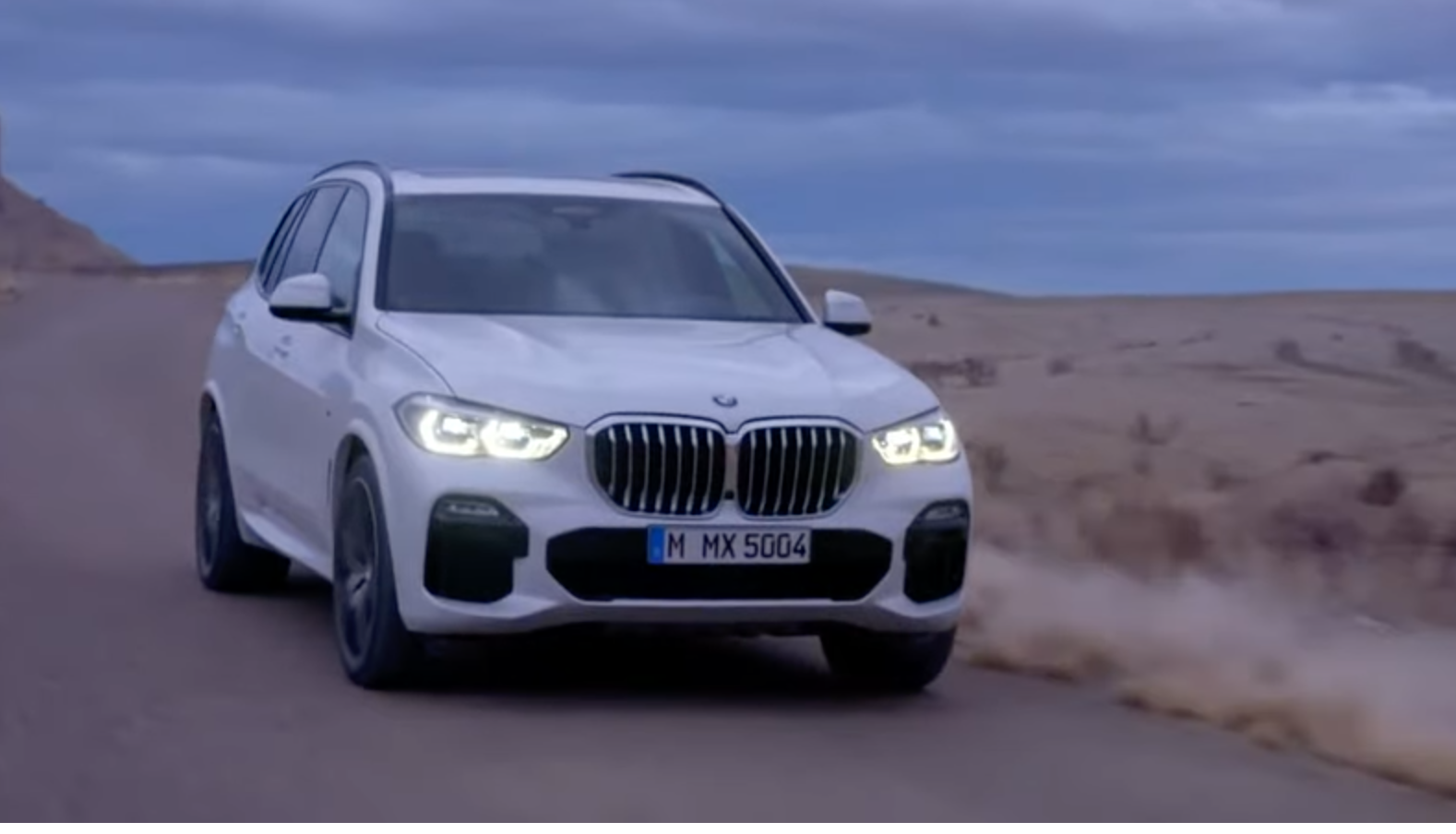 2023 BMW X5 in white driving down the road at dusk