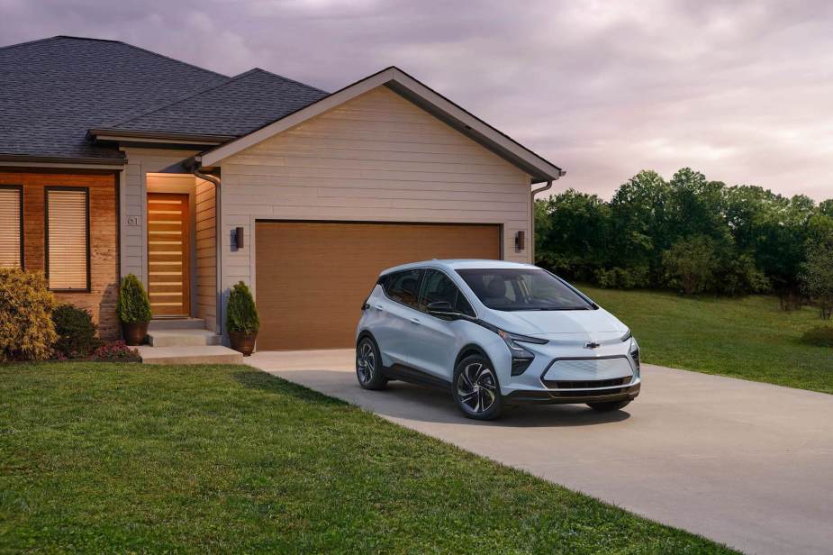 A light blue Chevrolet Bolt EV shows off its electric car styling and hatchback shape in house's driveway. 