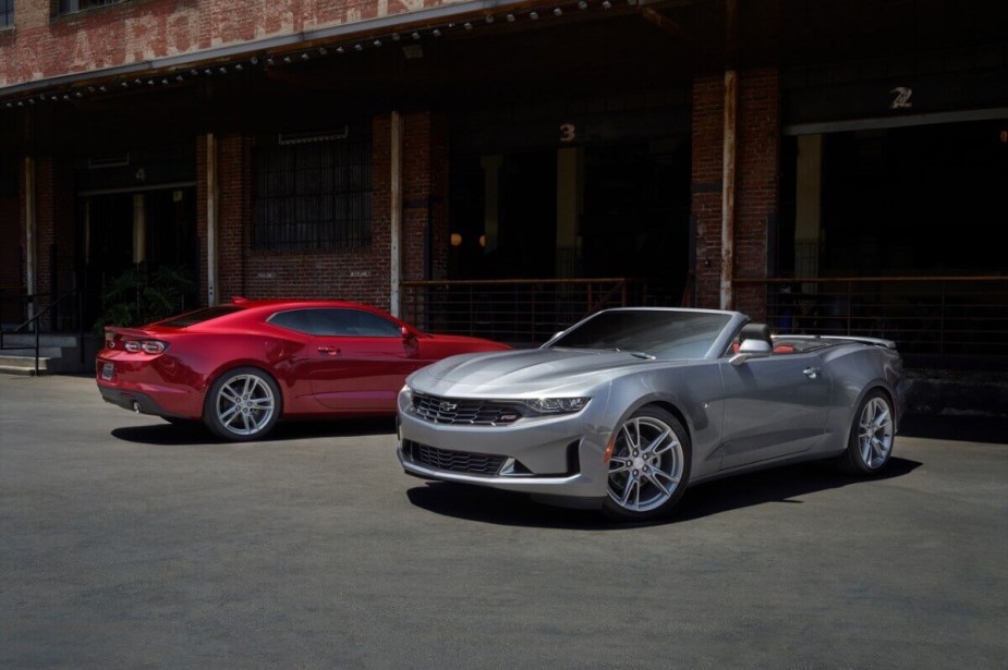 A Chevrolet Camaro coupe and convertible pose for a picture by a cheap hangar. 