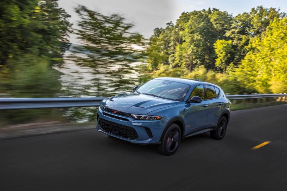 A blue-gray 2023 Dodge Hornet compact SUV model driving on a forest highway