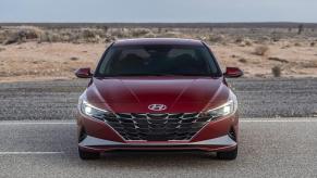 A new red 2023 Hyundai Elantra shows off its LED lights while it parks away from cars on a desert road.