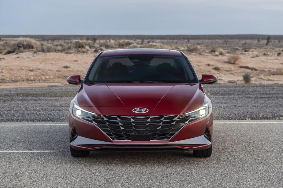 A new red 2023 Hyundai Elantra shows off its LED lights while it parks away from cars on a desert road. 