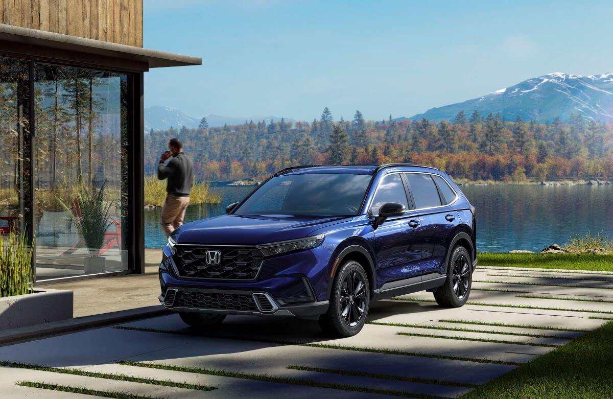 A dark blue 2023 Honda CR-V Sport Touring compact SUV model parked outside a luxury home near a forest lake