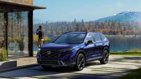 A dark blue 2023 Honda CR-V Sport Touring compact SUV model parked outside a luxury home near a forest lake