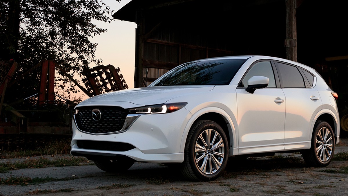 White 2023 Mazda CX-5 SUV parked in front of a barn