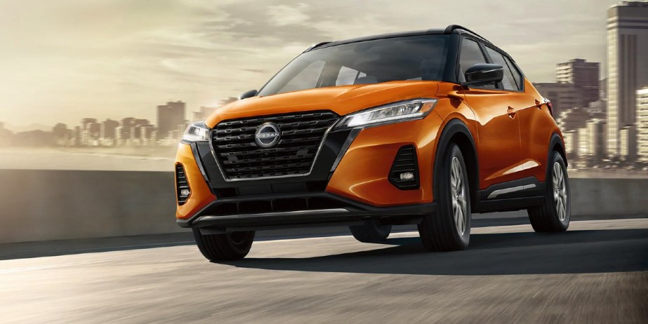 An orange 2023 Nissan Kicks subcompact SUV is driving on the road. 