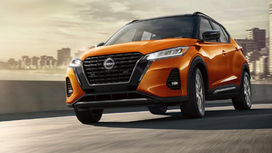 An orange Nissan Kicks subcompact SUV is driving on the road.