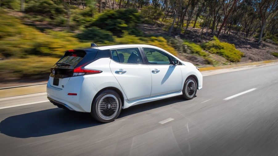 A white Nissan LEAF shows off its electric car proportions as it drives down a back road.