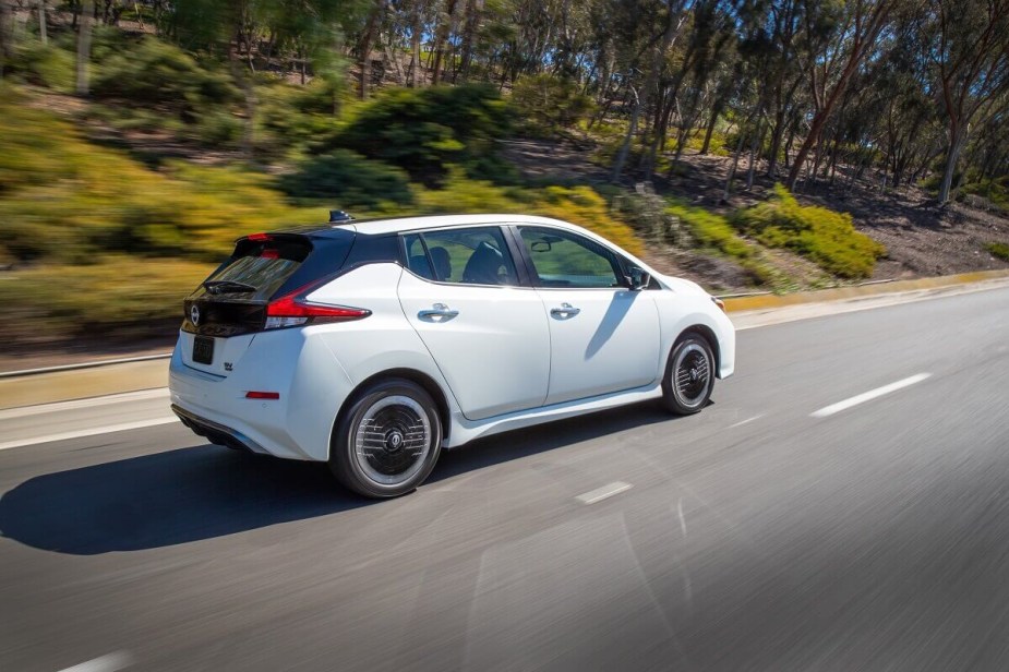 A white Nissan LEAF shows off its electric car proportions as it drives down a back road. 