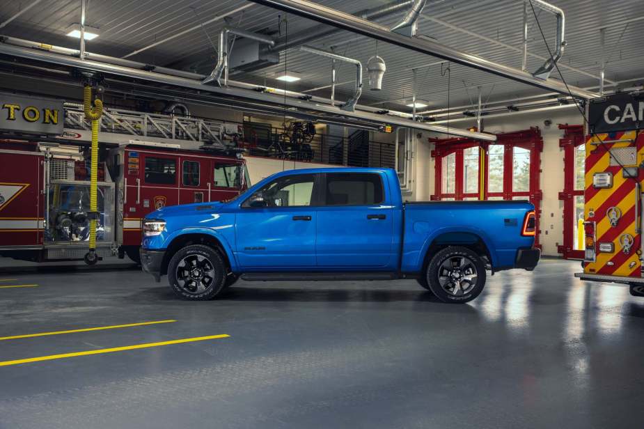 A side view of a bright blue Ram 1500 Longhorn with a crew cab configuration parked in a fire station.