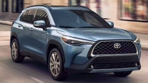 A blue 2023 Toyota Corolla Cross subcompact SUV is driving on the road.