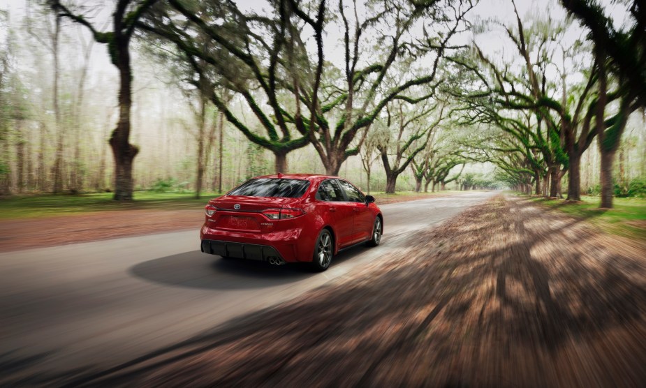 A red 2023 Toyota Corolla Hybrid cruises down a country road while it exercises its fuel-sipping efficiency. 