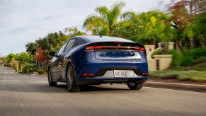 A new 2023 Toyota Prius shows off its blue color as it cruises down a country road.