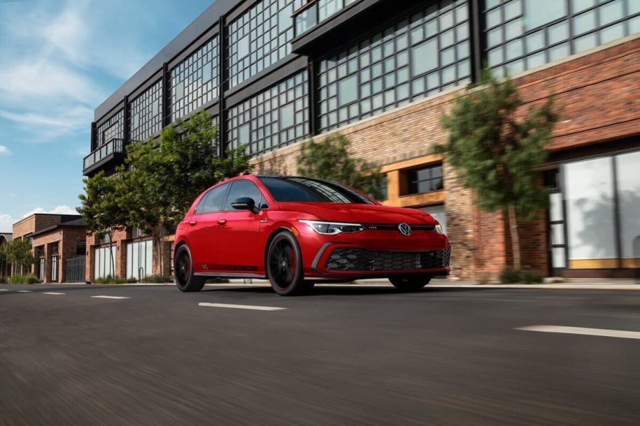 A red 2023 Volkswagen Golf GTI 40th Anniversary Edition shows off its celebratory German car paintwork and looks as it drives past an apartment building.