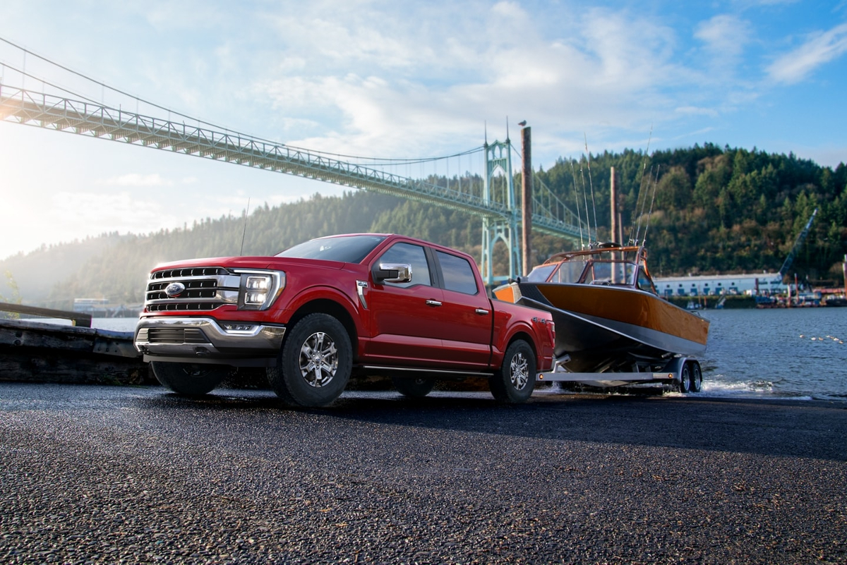 A red Ford F-150 tows a boat, it is a full-size truck that offers a V8 engine.