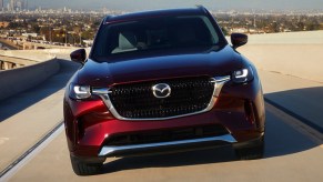 A red 2024 Mazda CX90 midsize SUV is driving on the road.