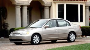 A seventh-generation 2001 Honda Civic sedan parked on a cobblestone road outside of a luxury home