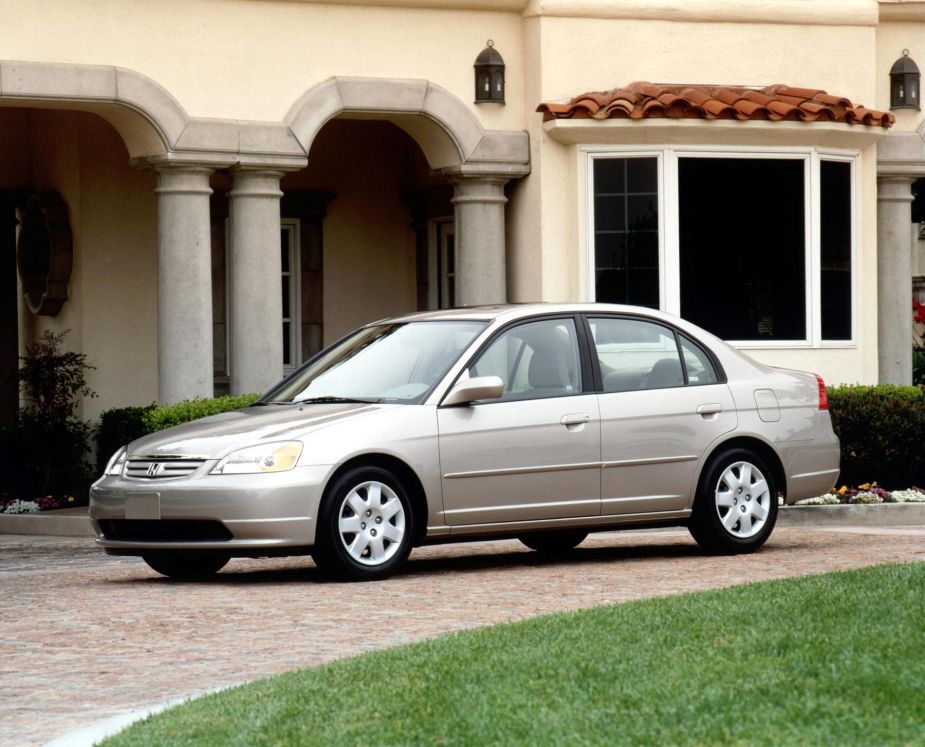 A seventh-generation 2001 Honda Civic sedan parked on a cobblestone road outside of a luxury home