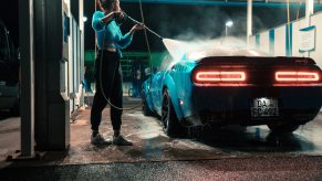 A woman uses a carwash spray gun to clean off a Dodge Challenger sports car at night.