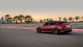 A red 2022 Alfa Romeo Giulia Quadrifoglio, like a Dodge Charger Hellcat, uses copious horsepower to attack a test track at sunset.