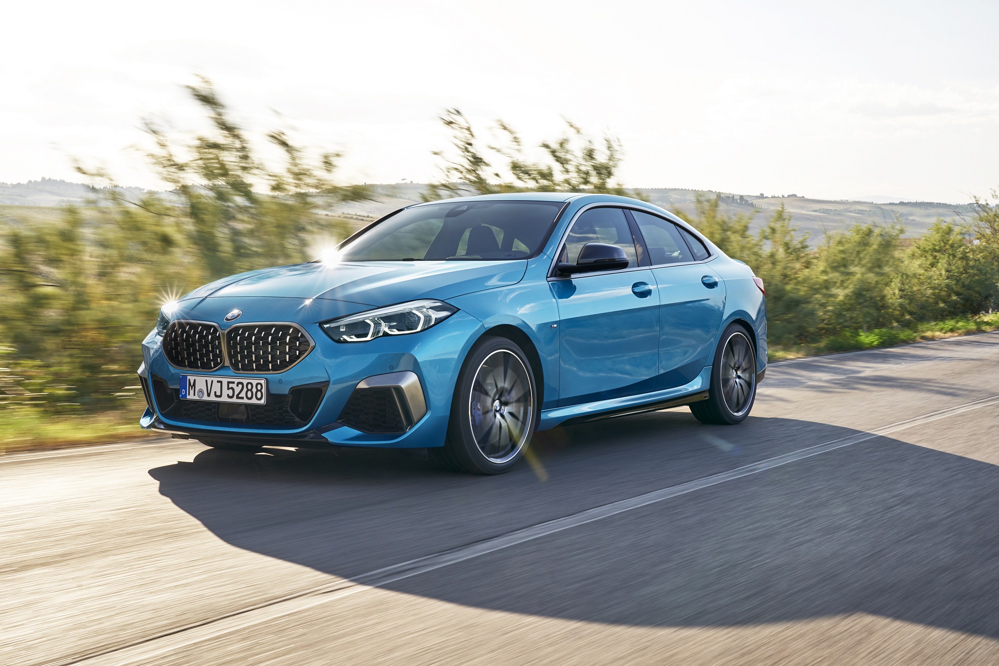 A new 2023 BMW 228i Gran Coupe drives down a coastal road in the sunlight.