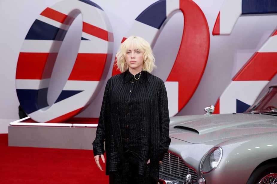 Billie Eilish poses next to the car from No Time to Die, an Aston Martin DB5. 