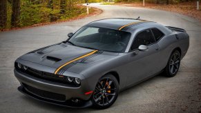 A 2023 Dodge Challenger shows off its striped gray paint work and muscle car styling on a back road.