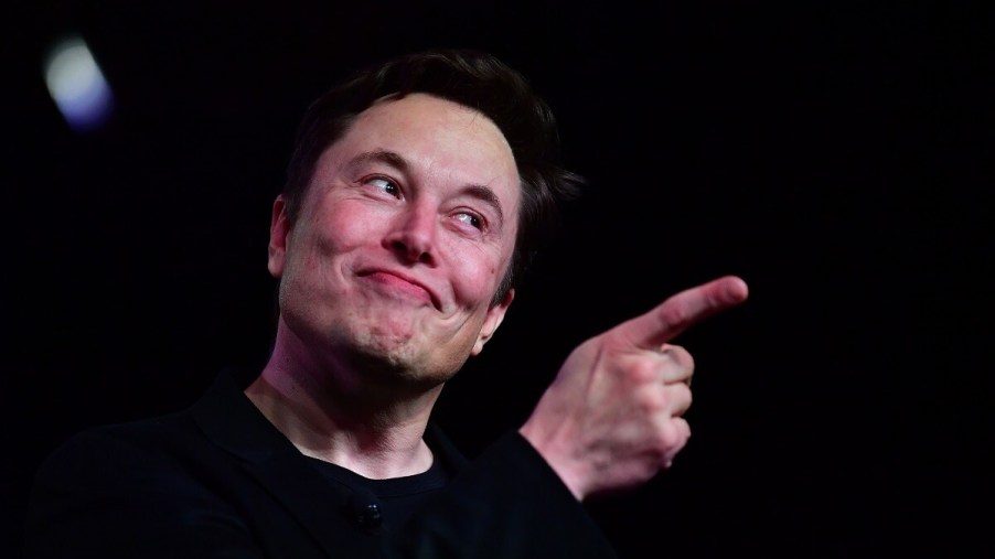 CEO Elon Musk makes a gesture at a Tesla in either California HQ2 or the Texas HQ.