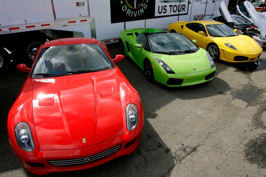 A red and yellow Ferrari are parked on either side of a bright green Lamborghini convertible at a supercar driving event.