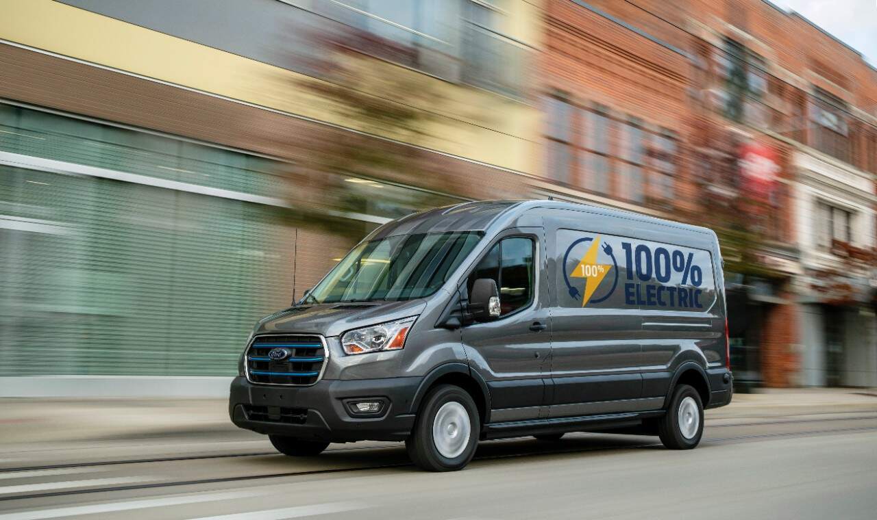 A Ford E-Transit electric commercial delivery van driving down the road.