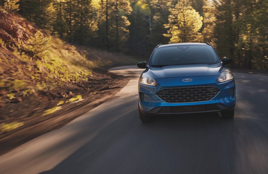 A blue Ford Escape driving down a wooded area, which is the Ford with the lowest insurance cost. 