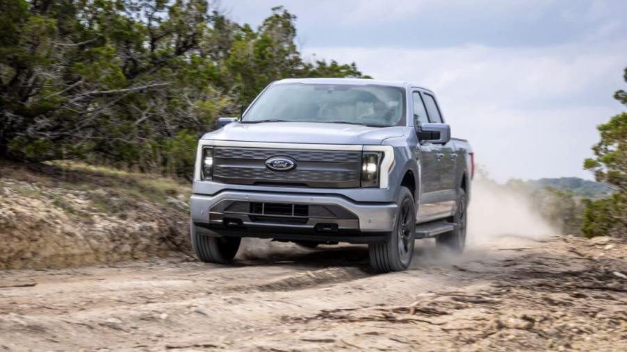 A Ford F-150 Lightning Lariat all-electric pickup truck model driving off-road on a worn dirt trail