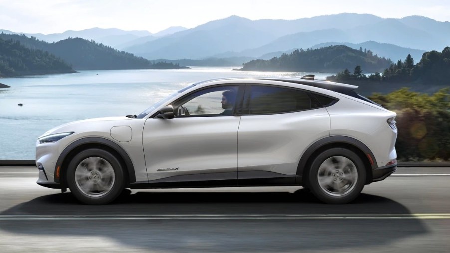 A white 2023 Ford Mustang Mach-E small electric SUV is driving on the road.