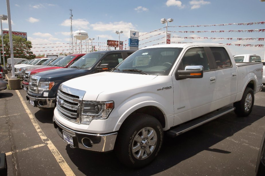 A white 2013 Ford F-150 sits at a dealership, it is a cheap and reliable full-size truck.