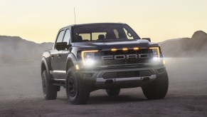 A Ford F-150 Raptor parked in the dirt with its lights on