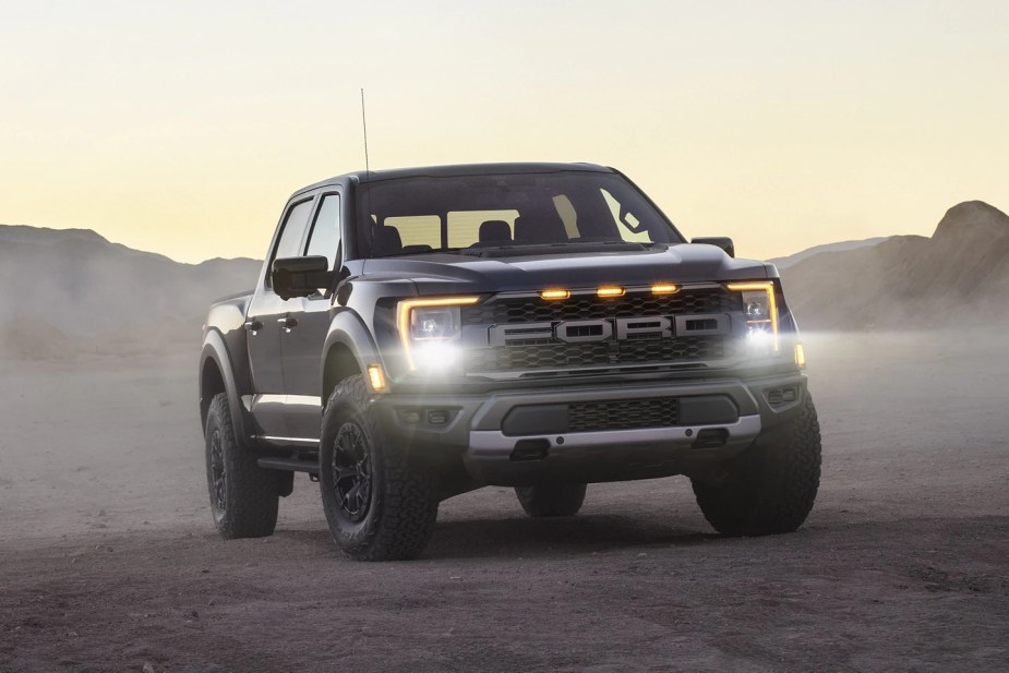 A Ford F-150 Raptor parked in the dirt with its lights on