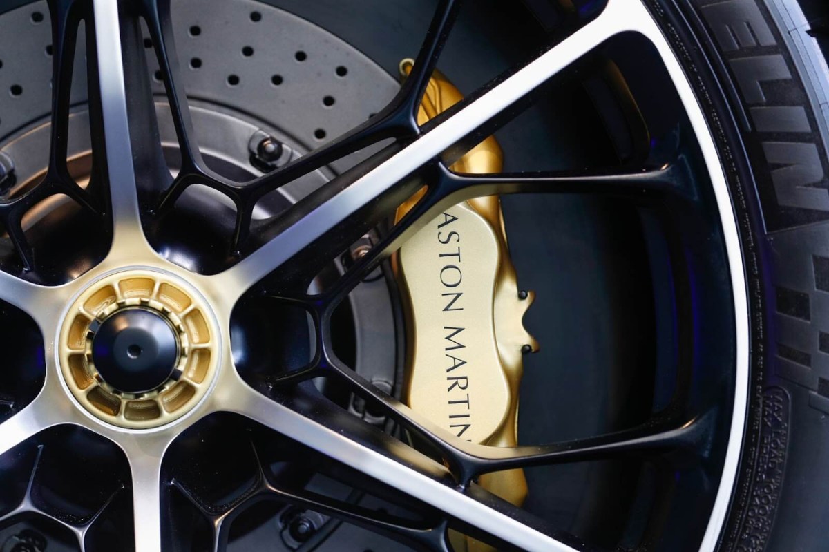 A gold painted Aston Martin brake caliper behind a mesh spoke wheel