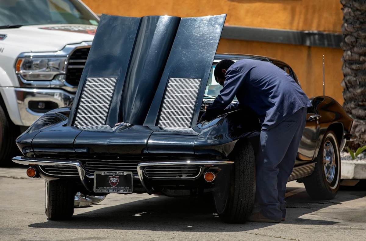 A mechanic looks under the hood of an antique car