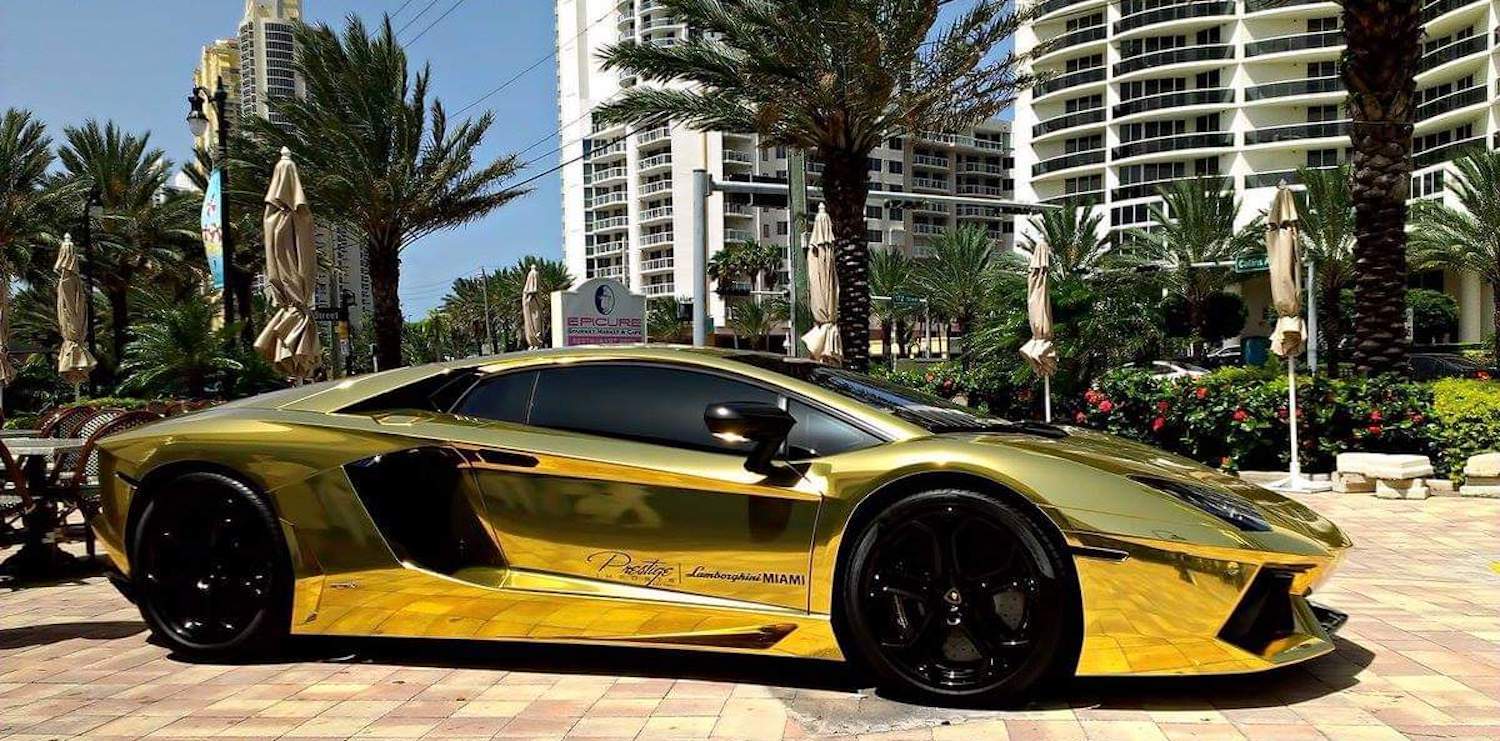 Gold-plated Lamborghini Gallardo supercar parked in front of a high-rise and palm trees in Florida.