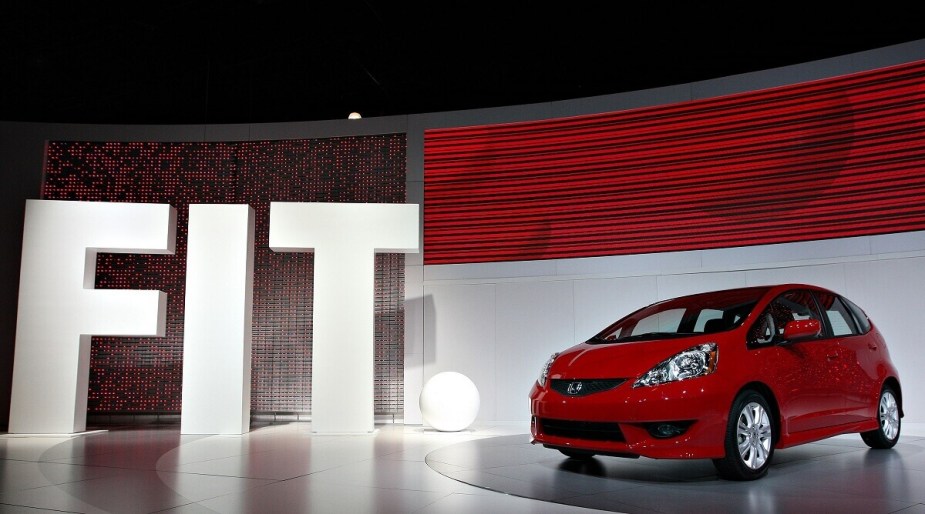 A red Honda Fit poses on stage at a car show, showing off its smaller dimensions than the Civic. 