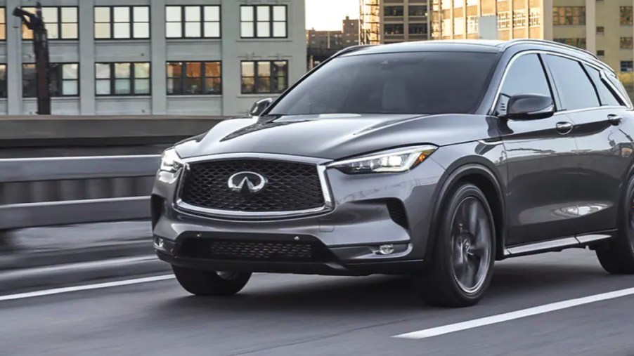 A gray 2023 Infiniti QX50 small luxury SUV is driving on the road.