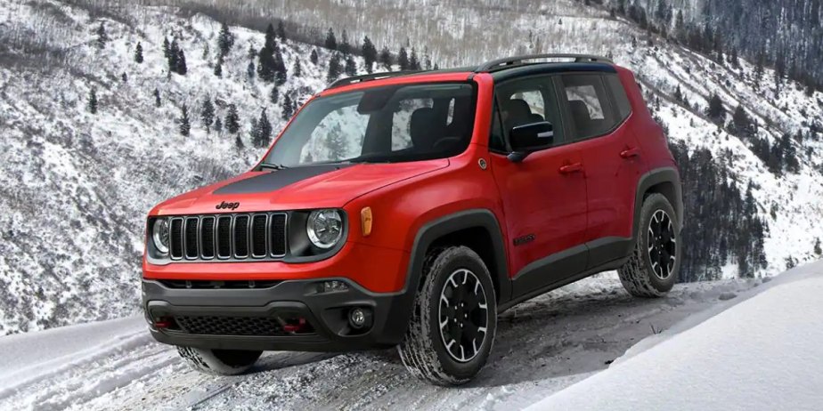 A red 2023 Jeep Renegade Trailhawk is driving in the snow. 