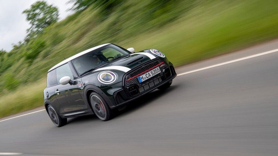 A MINI Cooper John Cooper Works hatchback blasts down a back road while it shows off its stripes.