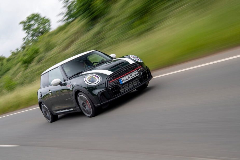 A MINI Cooper John Cooper Works hatchback blasts down a back road while it shows off its stripes.