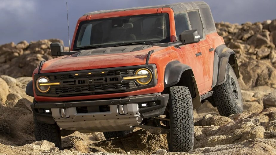 Orange 2023 Ford Bronco Raptor driving off-road over rocks